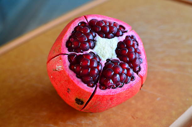 Opened fresh pomegranate showing red pulps and seeds on wood board with soft, blur background